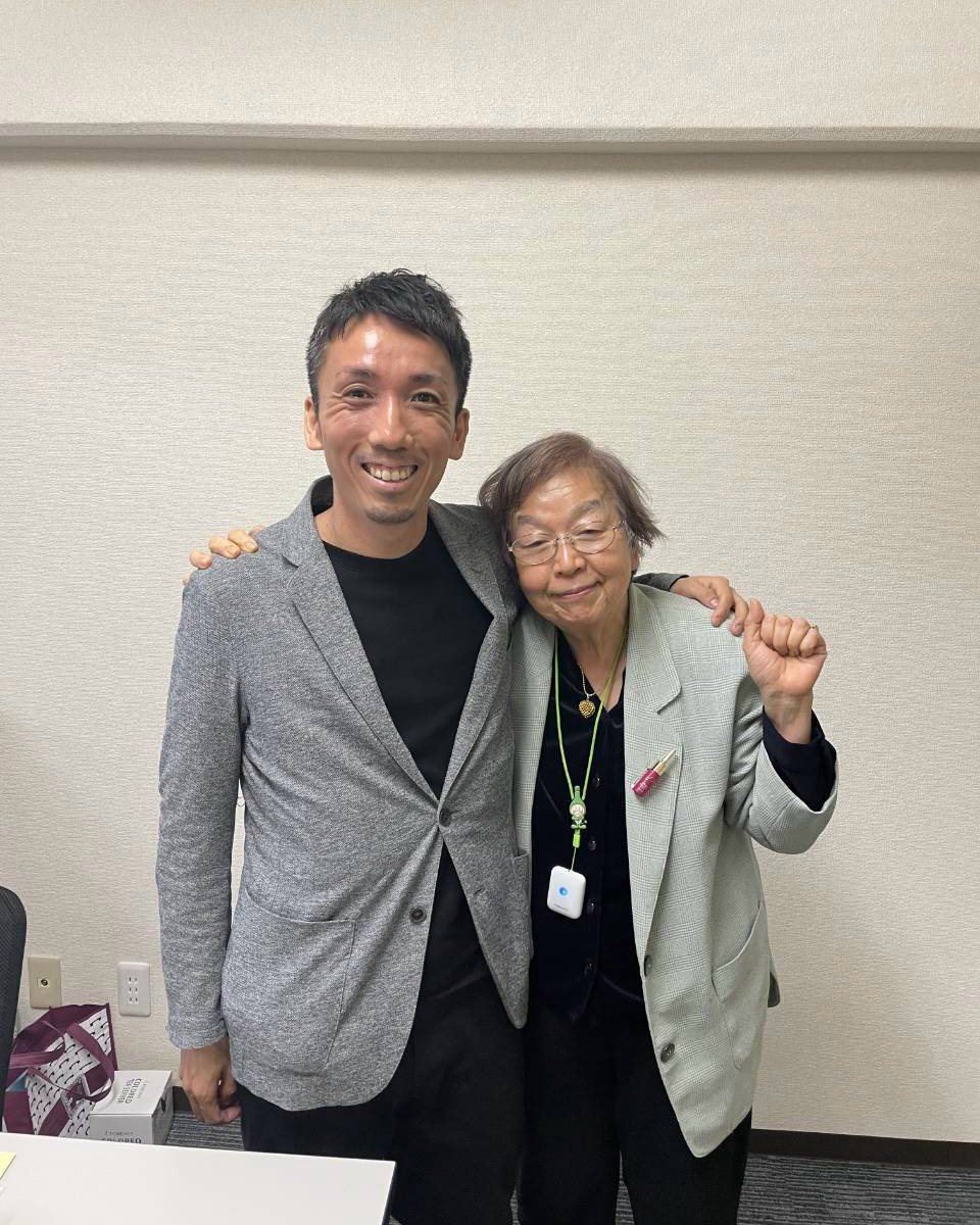 会議室で、侑二と肩を組み、こぶしを上げて笑うますみ